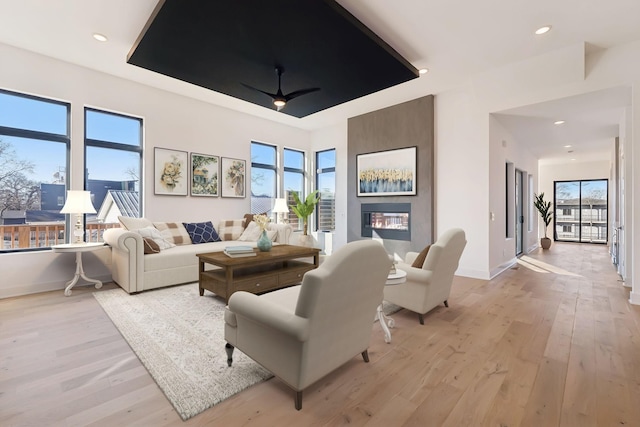 living room with ceiling fan, a large fireplace, and light wood-type flooring