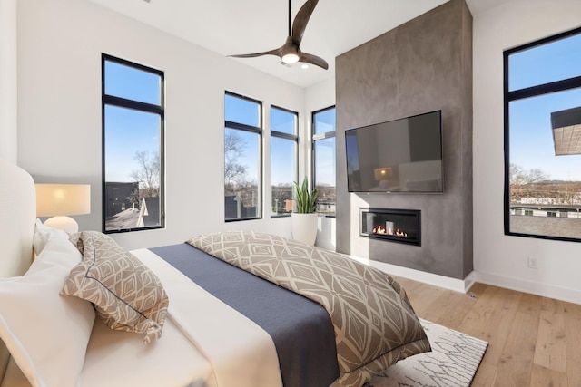 bedroom featuring light wood-type flooring, a large fireplace, and ceiling fan