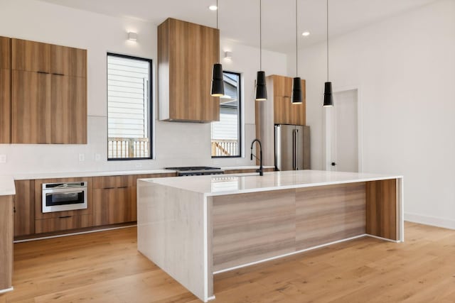 kitchen with a kitchen island with sink, pendant lighting, stainless steel appliances, and light hardwood / wood-style floors