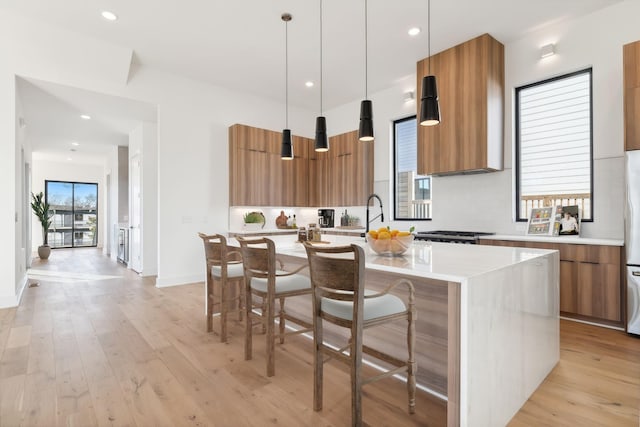 kitchen with a kitchen breakfast bar, extractor fan, light hardwood / wood-style floors, decorative light fixtures, and a center island with sink