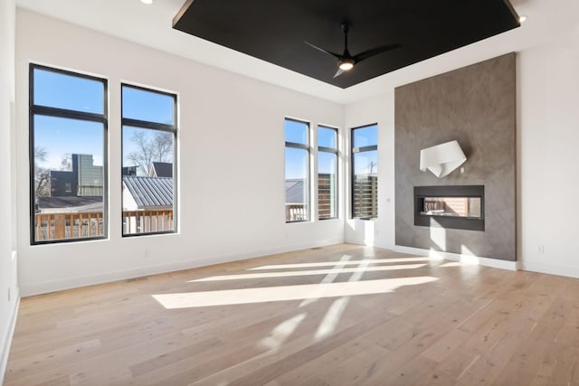 spare room with a multi sided fireplace, light wood-type flooring, a raised ceiling, and ceiling fan