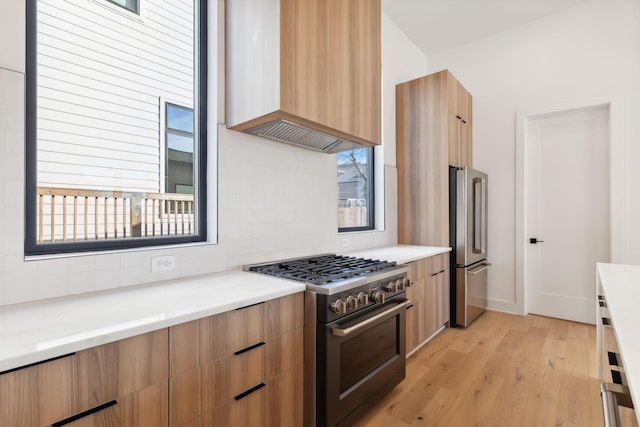 kitchen with tasteful backsplash, wall chimney exhaust hood, light hardwood / wood-style floors, and appliances with stainless steel finishes