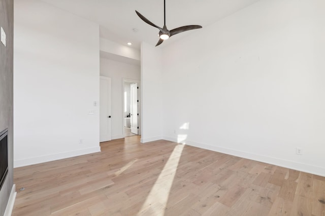 empty room with ceiling fan, a towering ceiling, and light hardwood / wood-style flooring