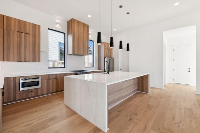 kitchen with pendant lighting, a large island with sink, oven, light stone countertops, and tasteful backsplash