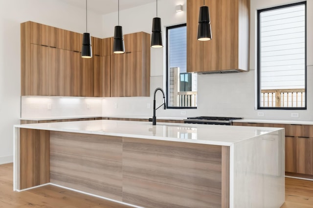 kitchen with light stone counters, light hardwood / wood-style flooring, an island with sink, pendant lighting, and extractor fan