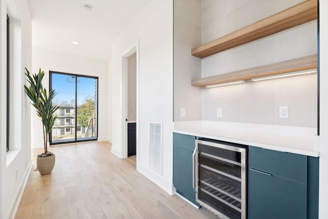 bar featuring blue cabinetry, beverage cooler, and light hardwood / wood-style flooring