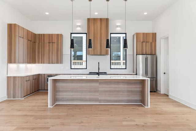 kitchen with sink, light hardwood / wood-style flooring, pendant lighting, high quality fridge, and a kitchen island with sink