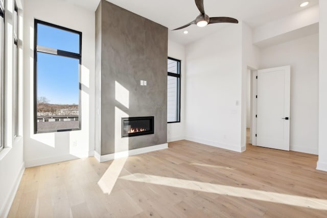 unfurnished living room featuring a large fireplace, light hardwood / wood-style flooring, and ceiling fan