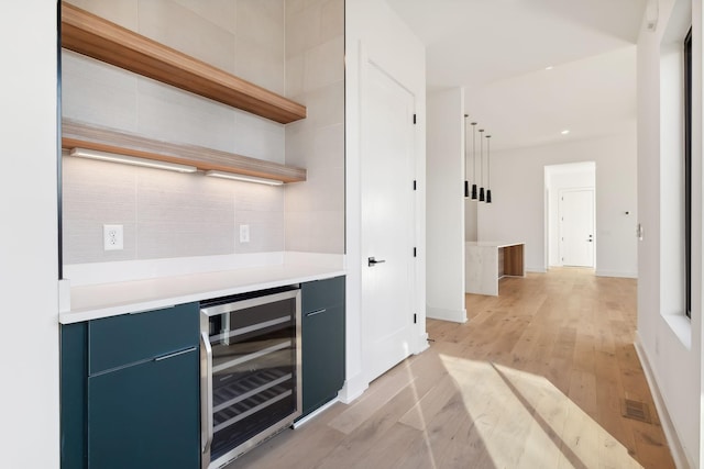 bar featuring light wood-type flooring, blue cabinets, and beverage cooler