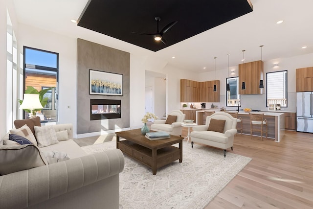 living room featuring a multi sided fireplace, ceiling fan, plenty of natural light, and light wood-type flooring