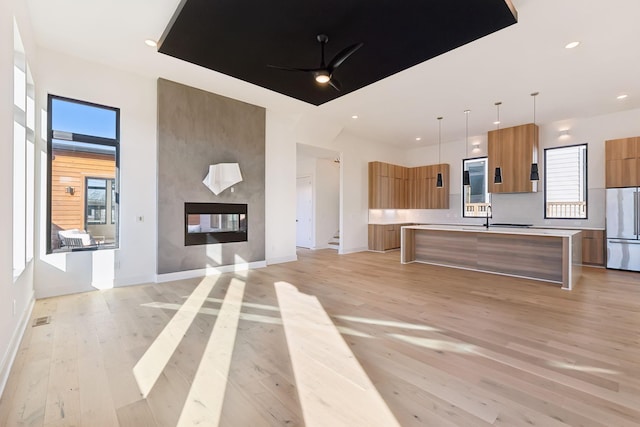 kitchen featuring a center island with sink, a multi sided fireplace, hanging light fixtures, ceiling fan, and stainless steel built in refrigerator