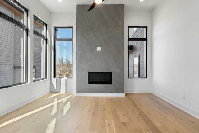 unfurnished living room with ceiling fan, a large fireplace, and light hardwood / wood-style flooring