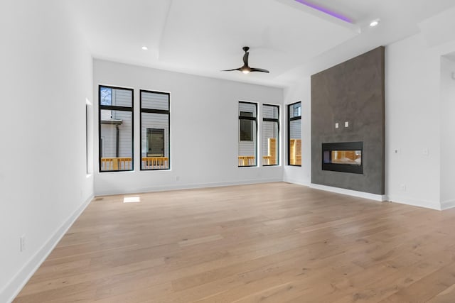 unfurnished living room with ceiling fan, a multi sided fireplace, and light wood-type flooring