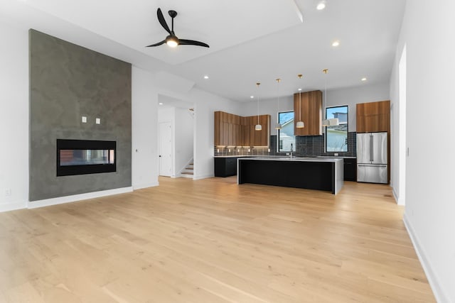 kitchen with stainless steel fridge, an island with sink, pendant lighting, a breakfast bar area, and decorative backsplash