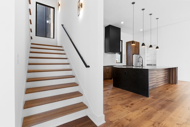 kitchen with sink, hanging light fixtures, light hardwood / wood-style flooring, stainless steel fridge, and an island with sink