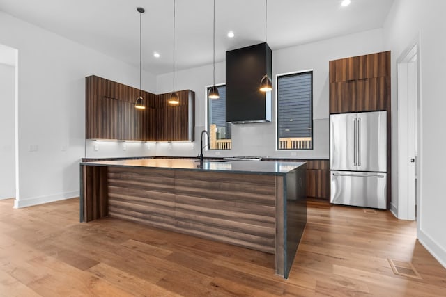 kitchen featuring light wood-type flooring, wall chimney exhaust hood, pendant lighting, a kitchen island, and stainless steel refrigerator