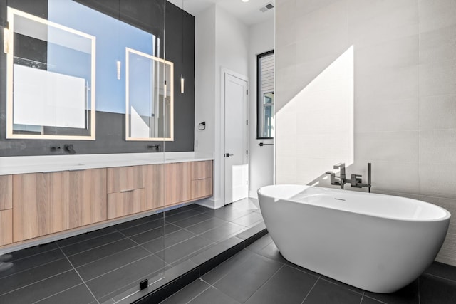 bathroom featuring tile patterned floors, a tub, vanity, and tile walls