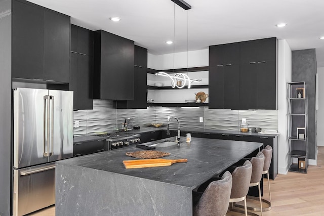 kitchen with light wood-type flooring, an island with sink, stainless steel refrigerator, and sink