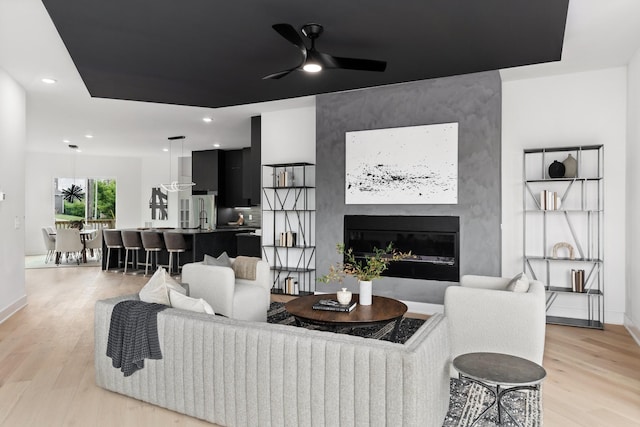 living room with a fireplace, ceiling fan, and light hardwood / wood-style flooring