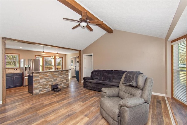 living room with ceiling fan with notable chandelier, wood-type flooring, vaulted ceiling with beams, and a healthy amount of sunlight