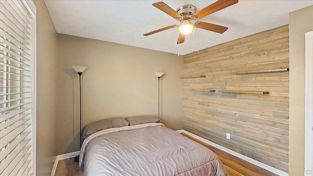 bedroom with hardwood / wood-style floors, ceiling fan, and wooden walls