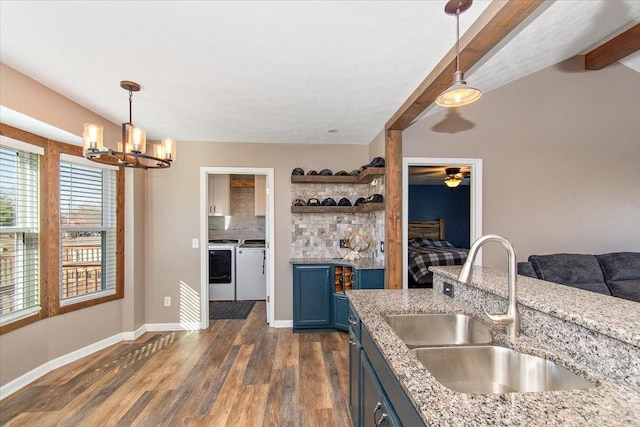 kitchen featuring washing machine and clothes dryer, beam ceiling, sink, blue cabinets, and decorative light fixtures