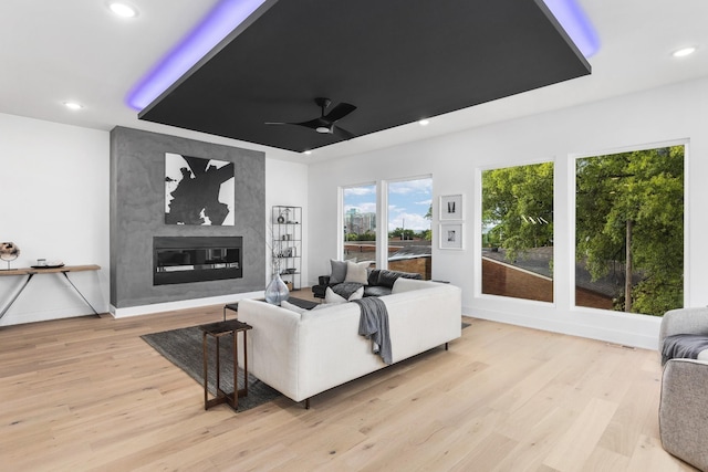 living room with ceiling fan, a large fireplace, and light hardwood / wood-style flooring