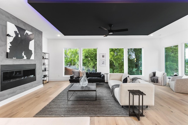 living room with light hardwood / wood-style floors, a raised ceiling, ceiling fan, and a fireplace