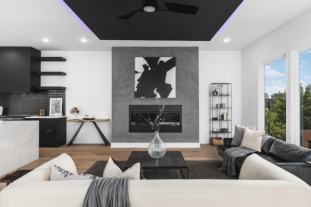 living room with a premium fireplace, wood-type flooring, and ceiling fan