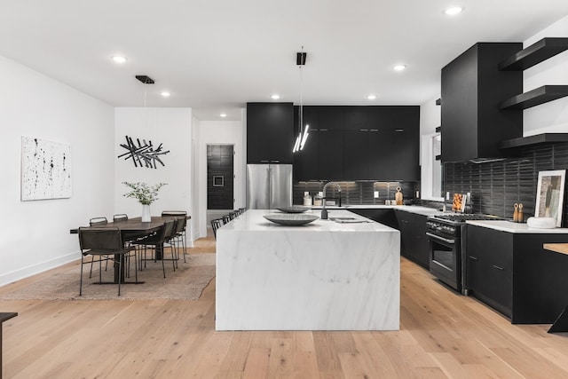 kitchen with pendant lighting, stainless steel appliances, an island with sink, decorative backsplash, and light hardwood / wood-style floors