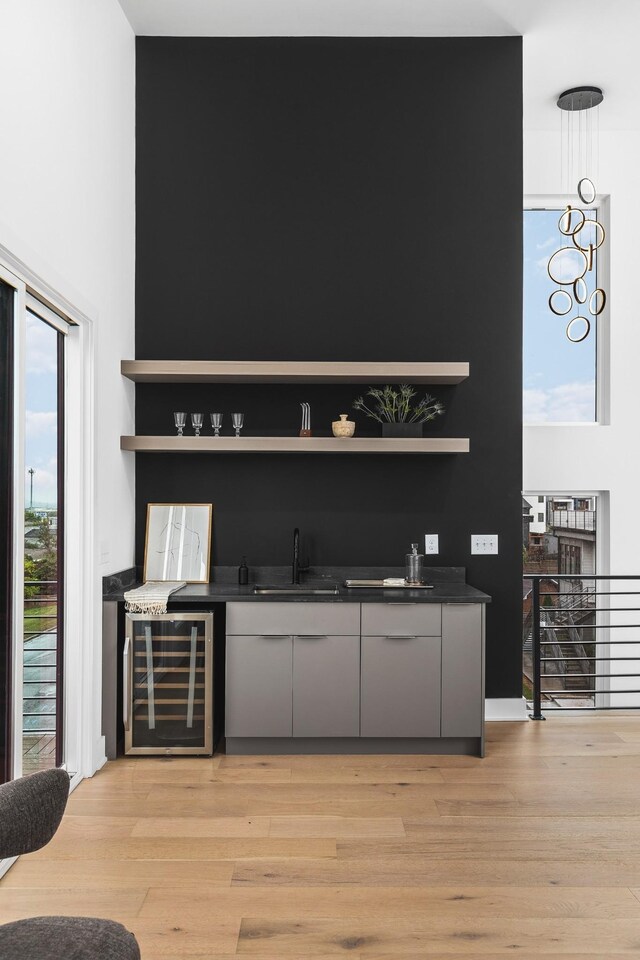 bar featuring sink, beverage cooler, gray cabinets, and light hardwood / wood-style floors