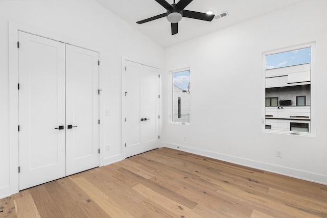 unfurnished bedroom with ceiling fan, multiple closets, light wood-type flooring, and lofted ceiling