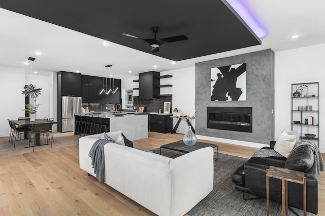 living room with ceiling fan, a fireplace, light hardwood / wood-style flooring, and sink