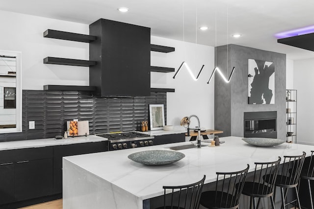 kitchen with a fireplace, stainless steel gas stovetop, decorative backsplash, sink, and a kitchen island with sink