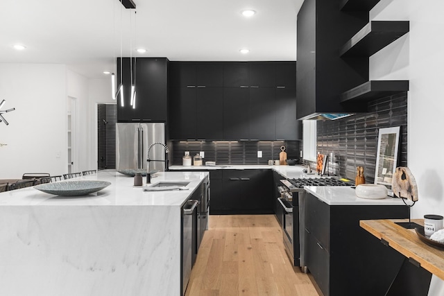 kitchen with appliances with stainless steel finishes, pendant lighting, tasteful backsplash, and an island with sink