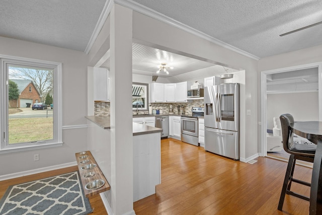 kitchen with white cabinetry, sink, stainless steel appliances, backsplash, and kitchen peninsula