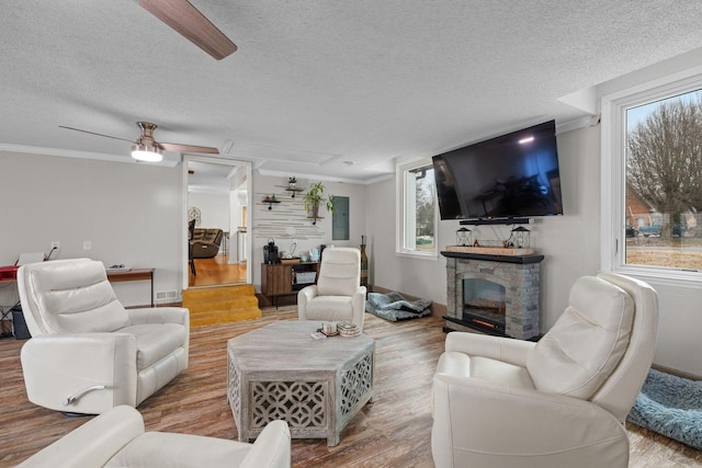 living room with a textured ceiling, crown molding, wood-type flooring, electric panel, and a stone fireplace