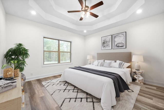 bedroom with hardwood / wood-style floors, ceiling fan, and a raised ceiling