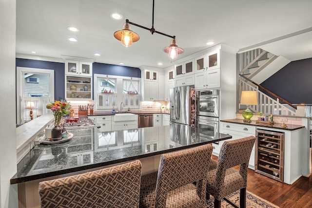 kitchen with wine cooler, a kitchen bar, kitchen peninsula, stainless steel appliances, and white cabinets