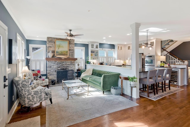 living room featuring ornate columns, hardwood / wood-style floors, ceiling fan, a fireplace, and crown molding