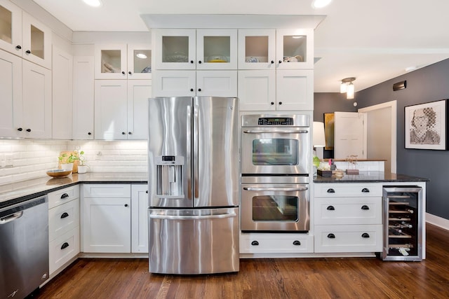 kitchen with dark wood-type flooring, appliances with stainless steel finishes, white cabinets, dark stone counters, and beverage cooler