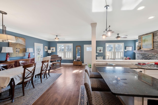 dining space with dark wood-type flooring, ceiling fan, crown molding, and a stone fireplace