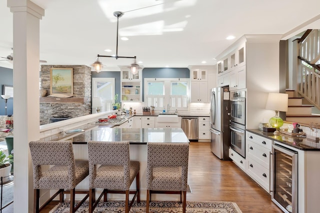 kitchen featuring kitchen peninsula, a breakfast bar area, stainless steel appliances, beverage cooler, and white cabinets