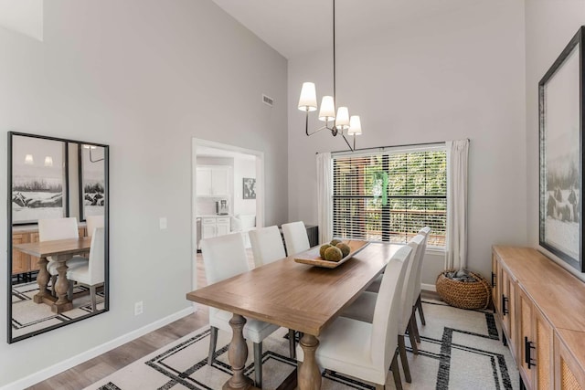 dining room featuring light wood-type flooring, a towering ceiling, and an inviting chandelier