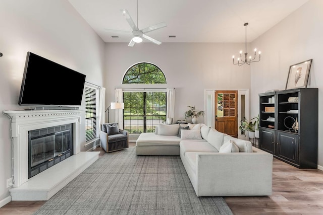 living room with a high ceiling, ceiling fan with notable chandelier, and light hardwood / wood-style flooring