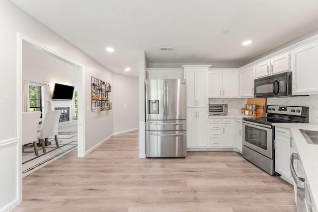 kitchen featuring tasteful backsplash, white cabinets, stainless steel appliances, and light hardwood / wood-style floors