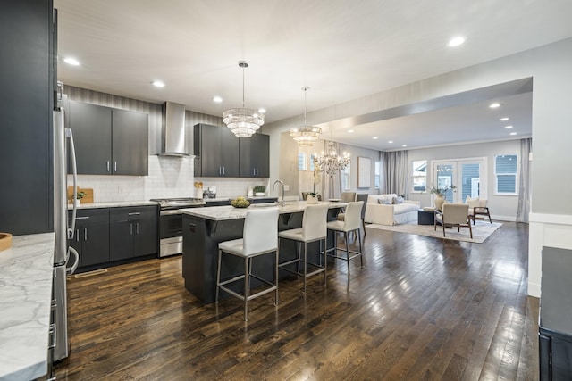 kitchen with gas stove, wall chimney range hood, a notable chandelier, pendant lighting, and decorative backsplash