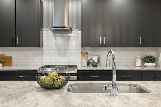 kitchen featuring light stone countertops, decorative backsplash, wall chimney exhaust hood, gas range, and sink