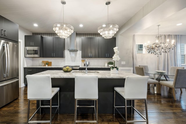 kitchen featuring stainless steel appliances, a center island with sink, wall chimney exhaust hood, and a notable chandelier