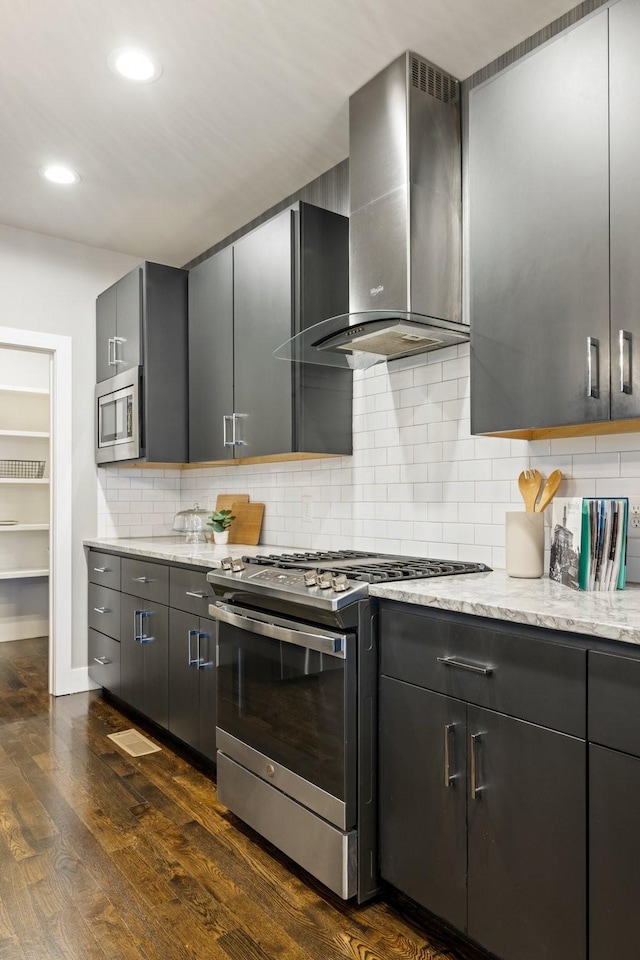 kitchen with decorative backsplash, light stone counters, wall chimney exhaust hood, stainless steel appliances, and dark wood-type flooring